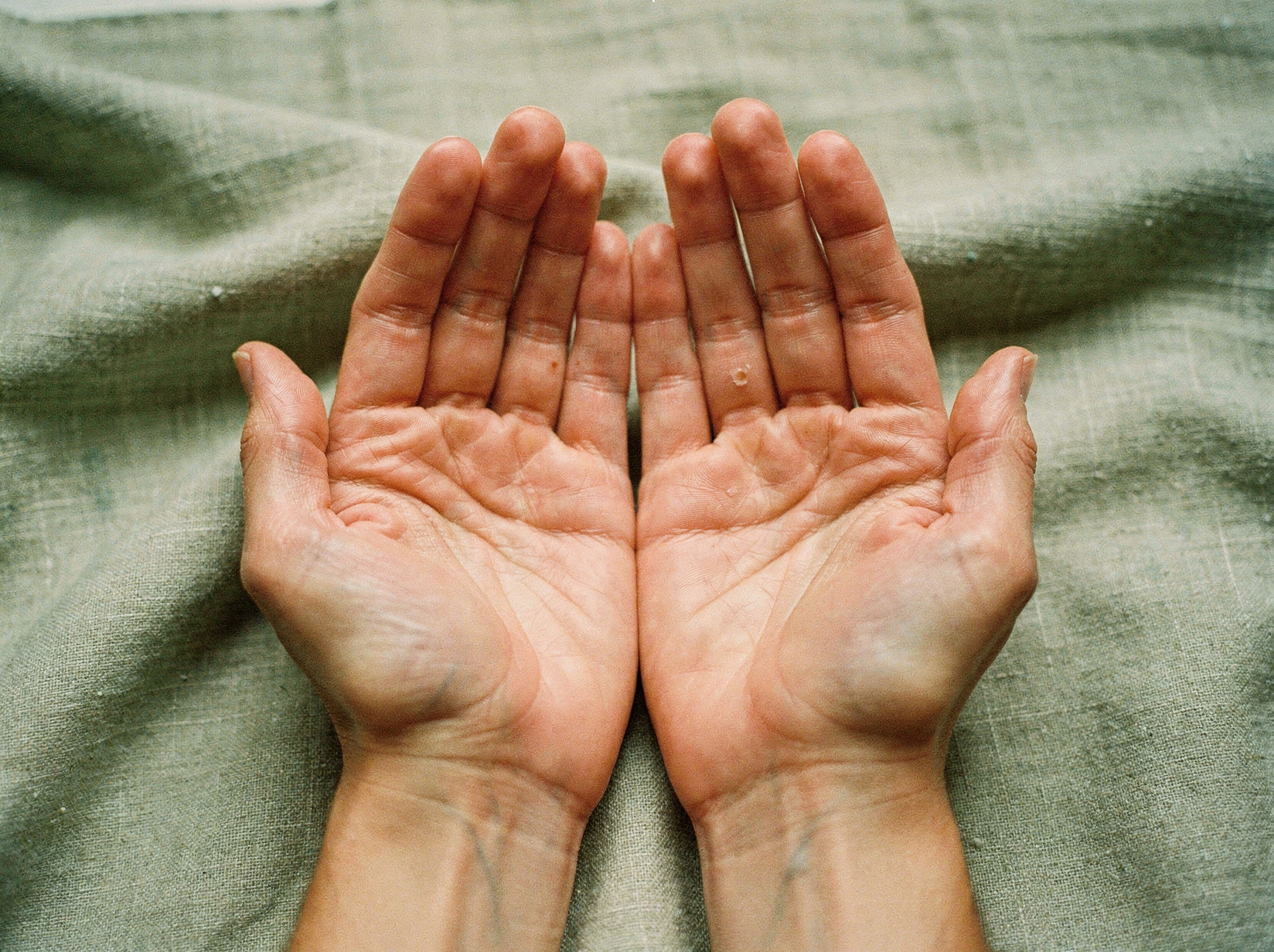 Open hands resting gently in a receiving gesture on natural sage linen